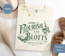 Load image into Gallery viewer, Folded ivory comfort colors t-shirt with 'Flourish and Blotts Booksellers' design on a white background.