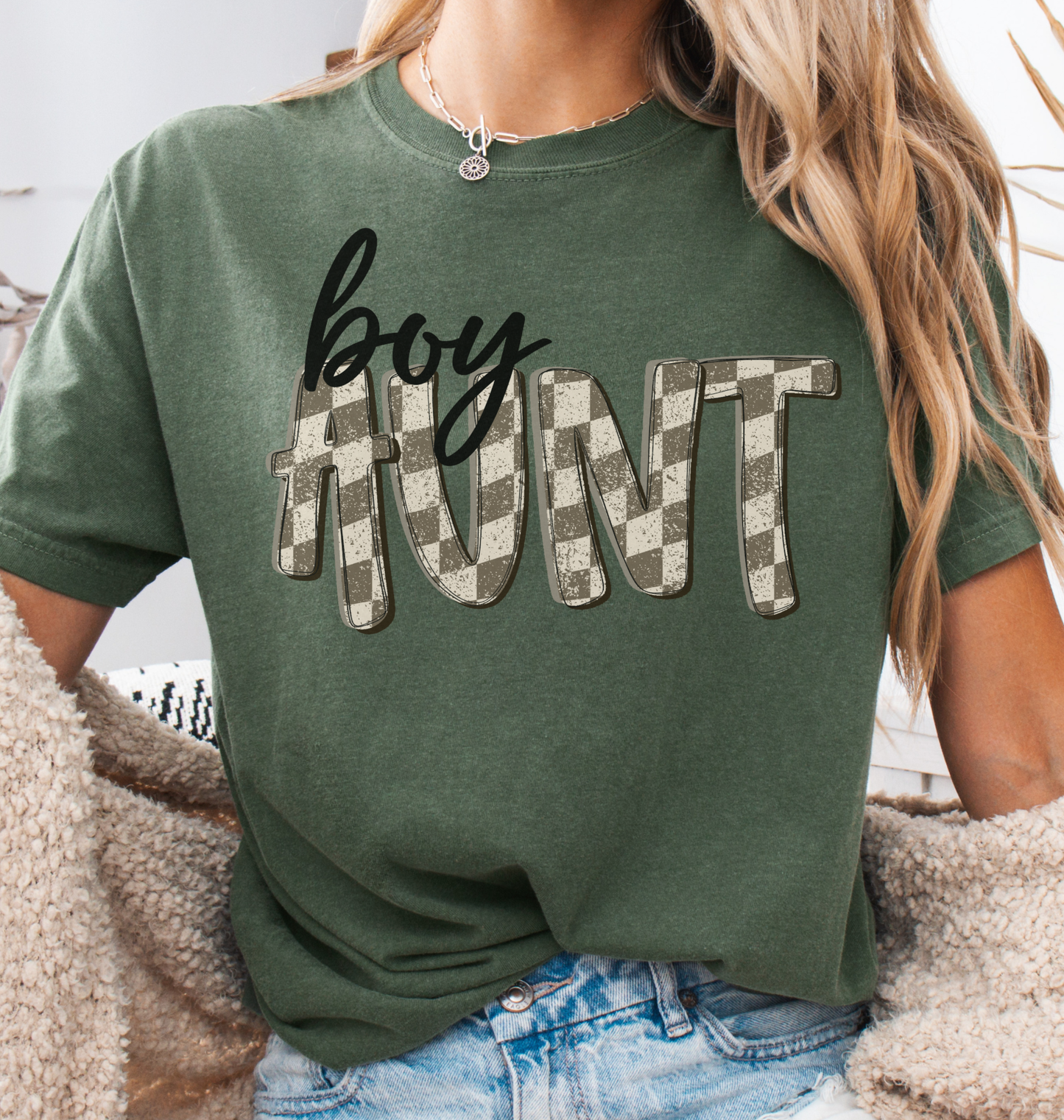 Woman wearing a moss green comfort colors t-shirt with retro checkered 'boy aunt' text.