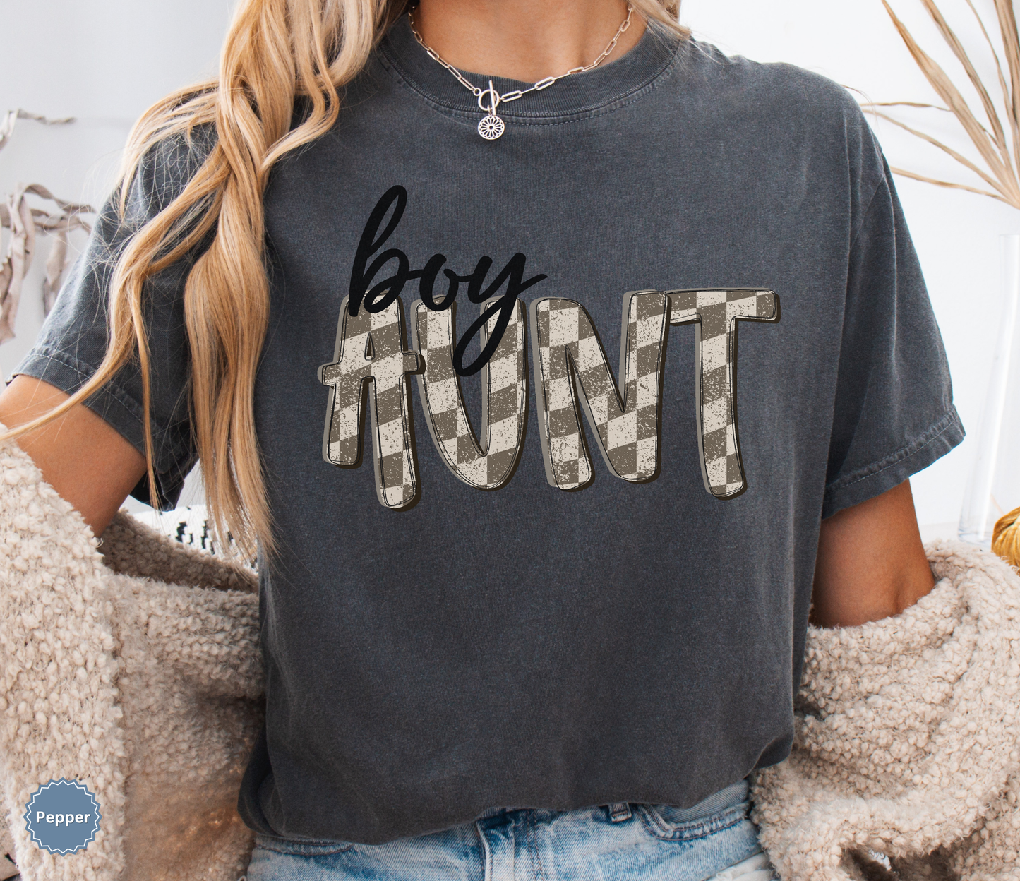 Woman wearing a dark grey pepper comfort colors t-shirt with retro checkered 'boy aunt' text.