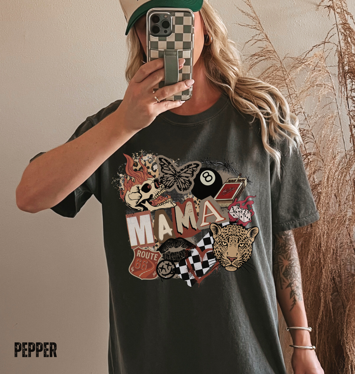 Woman wearing a dark gray pepper comfort colors t-shirt with a western style graphic 'MAMA' design with a skull, leopard and checkered patterns.