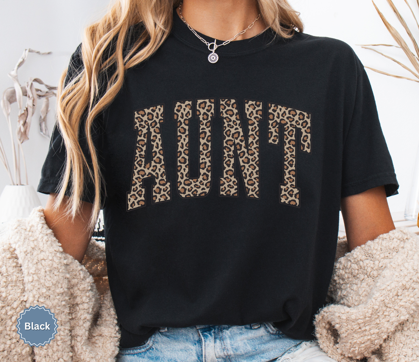 Woman wearing a black Comfort Colors t-shirt with leopard print 'AUNT' varsity text.