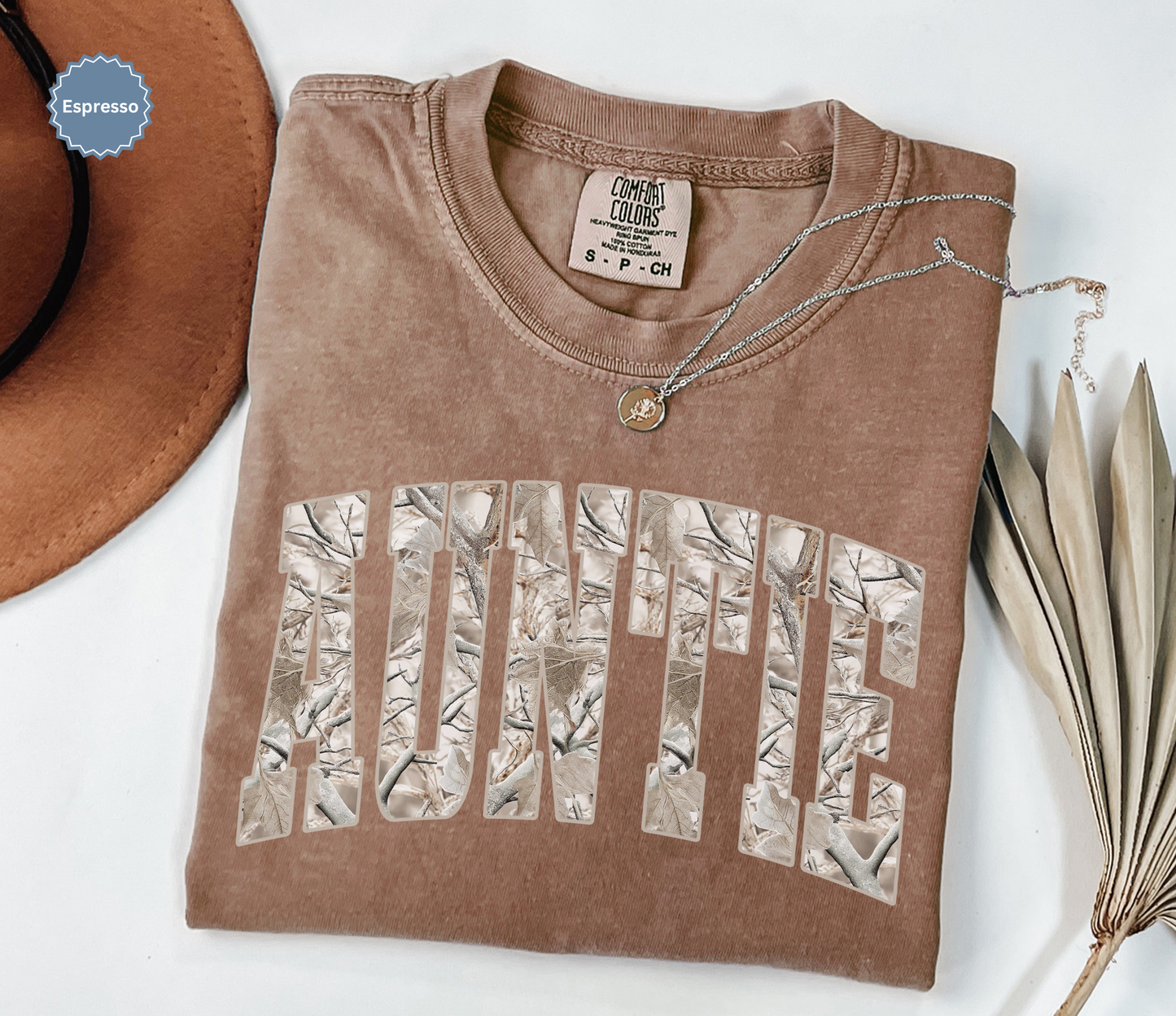 Folded comfort colors espresso brown t-shirt with 'Auntie' printed in a snow camo pattern.