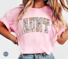 Load image into Gallery viewer, Comfort colors light pink blossom t-shirt with floral 'AUNT' varsity text
