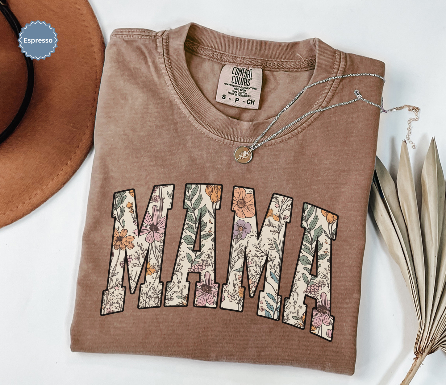 Folded brown T-shirt with a varsity style "MAMA" floral print. 