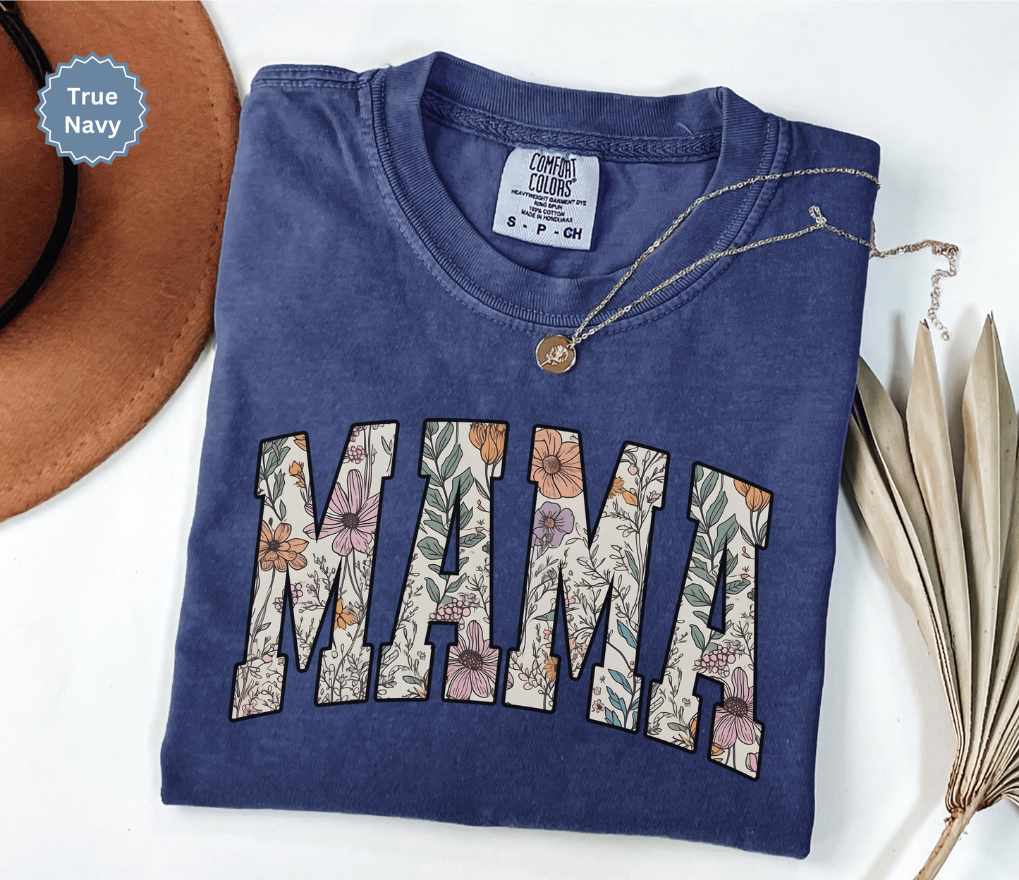 Folded navy blue T-shirt with a varsity style "MAMA" floral print. 