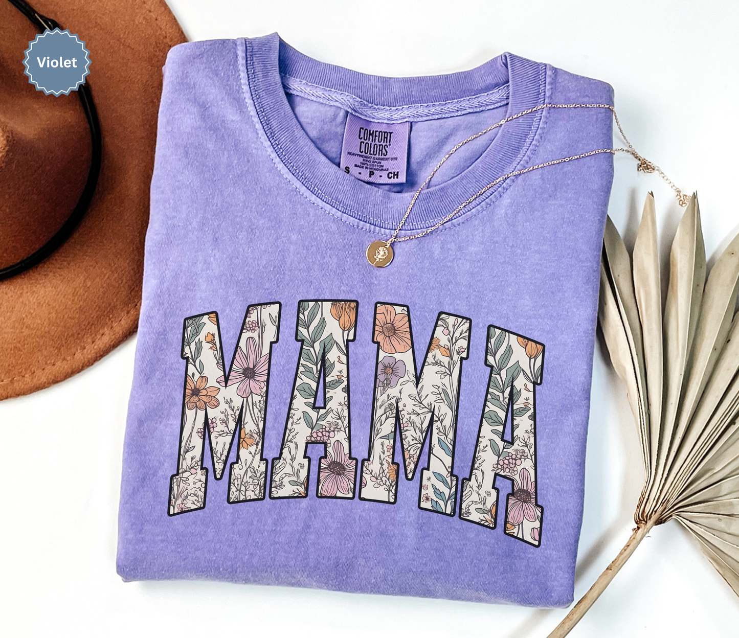Folded violet purple T-shirt with a varsity style "MAMA" floral print. 